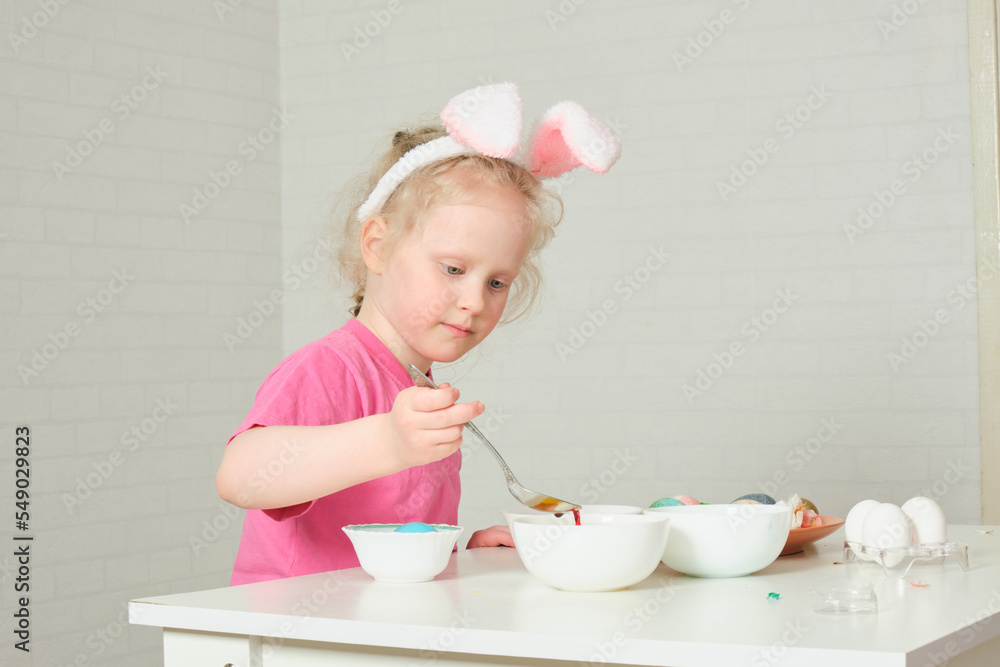 little girl in bunny ears , Easter concept, table with Easter eggs, celebrating Easter. little girl in bunny ears , Easter concept, table with Easter eggs, celebrating Easter.