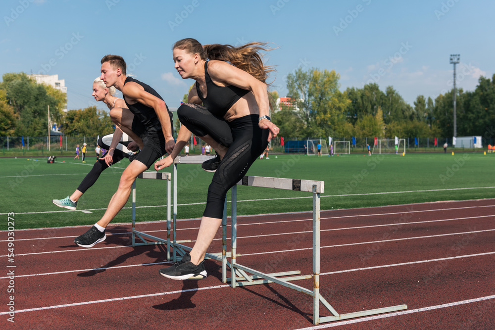 Two athlete woman and man runnner running hurdles at the stadium outdoors