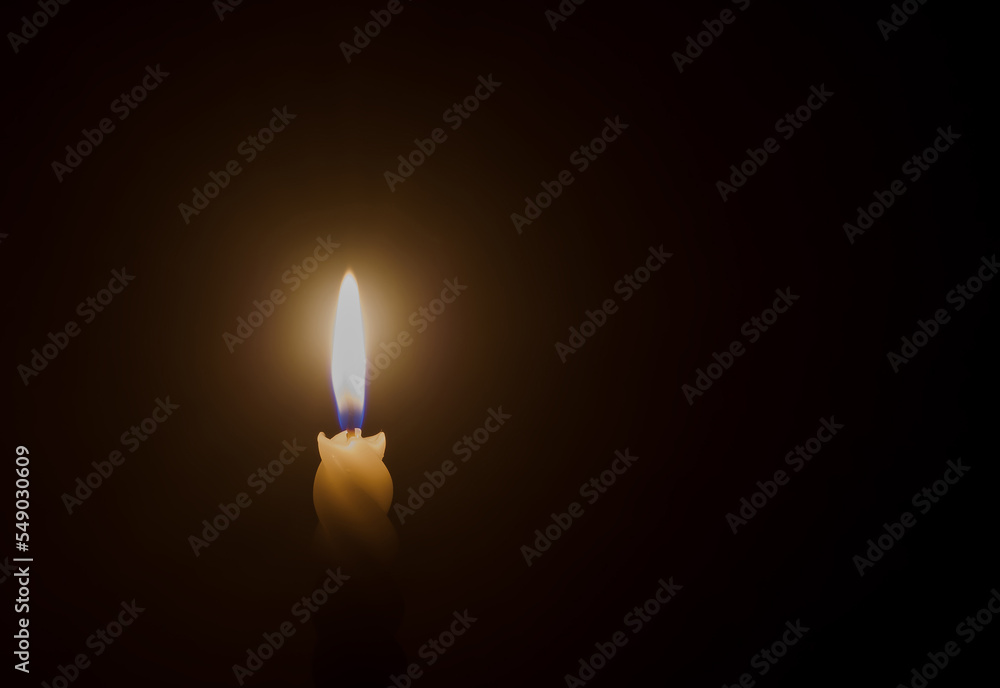 A single burning candle flame or light glowing on a spiral white candle on black or dark background on table in church for Christmas, funeral or memorial service A single burning candle flame or light glowing on a spiral white candle on black or dark background on table in church for Christmas, funeral or memorial service