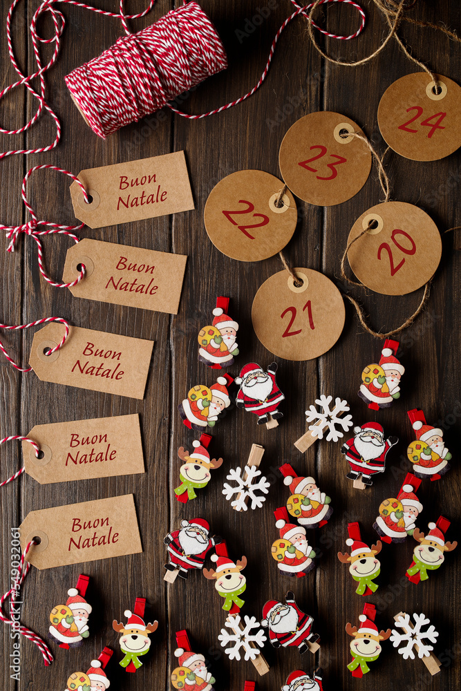 Christmas decorations: clothespins with Santa Claus, and snowflake decoration. Labels with dates for Advent calendar, and labels with  Italian language  ‘Buon Natale’ on wooden table.