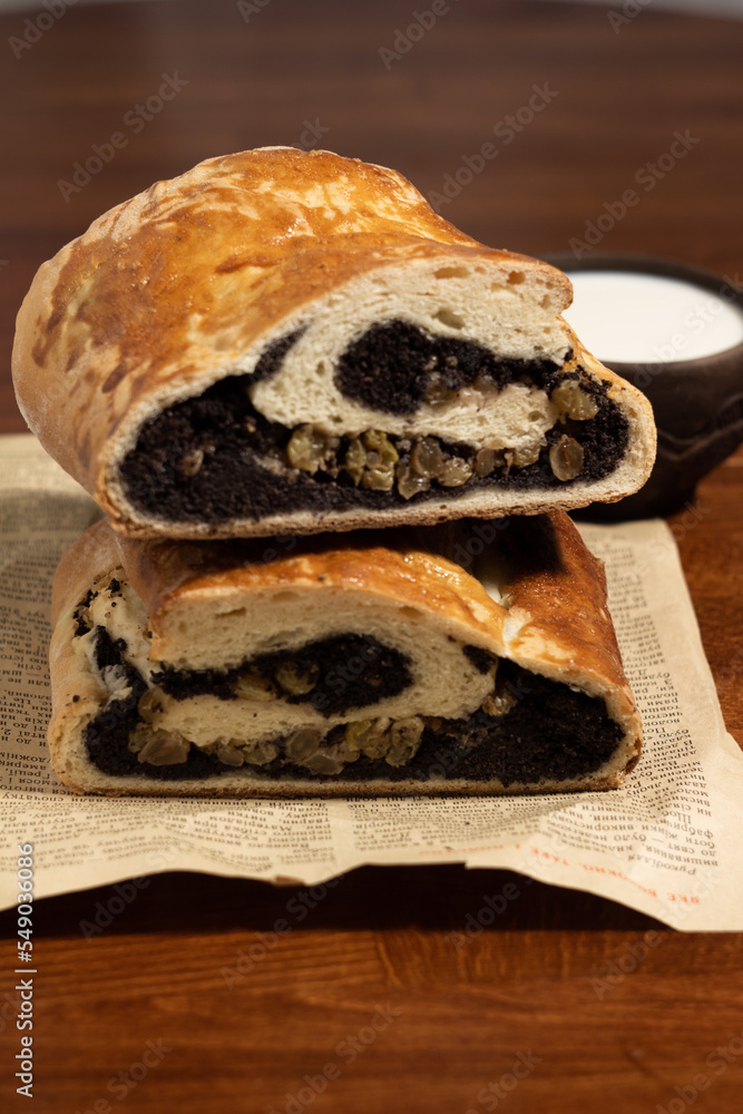 vertical photo of a ruddy poppy seed roll on a piece of old newspaper with a black clay cup filled with milk on a dark wooden table vertical photo of a ruddy poppy seed roll on a piece of old newspaper with a black clay cup filled with milk on a dark wooden table
