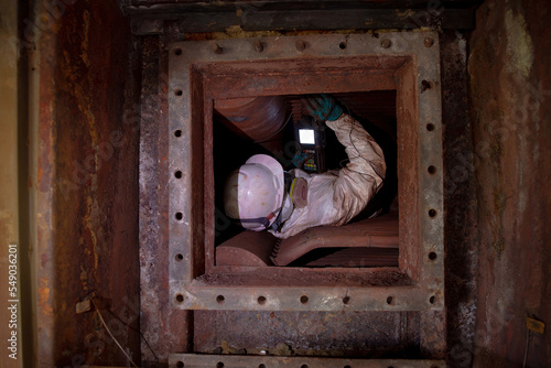 Male inspector wearing chemical protective clothing working to measure thickness in confined space