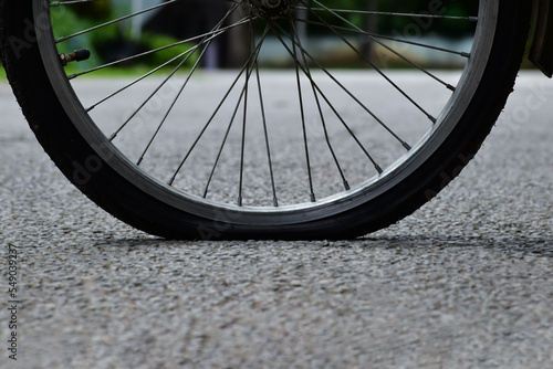 Rear wheel of bike which is flat and parked on the pavement beside the road. 