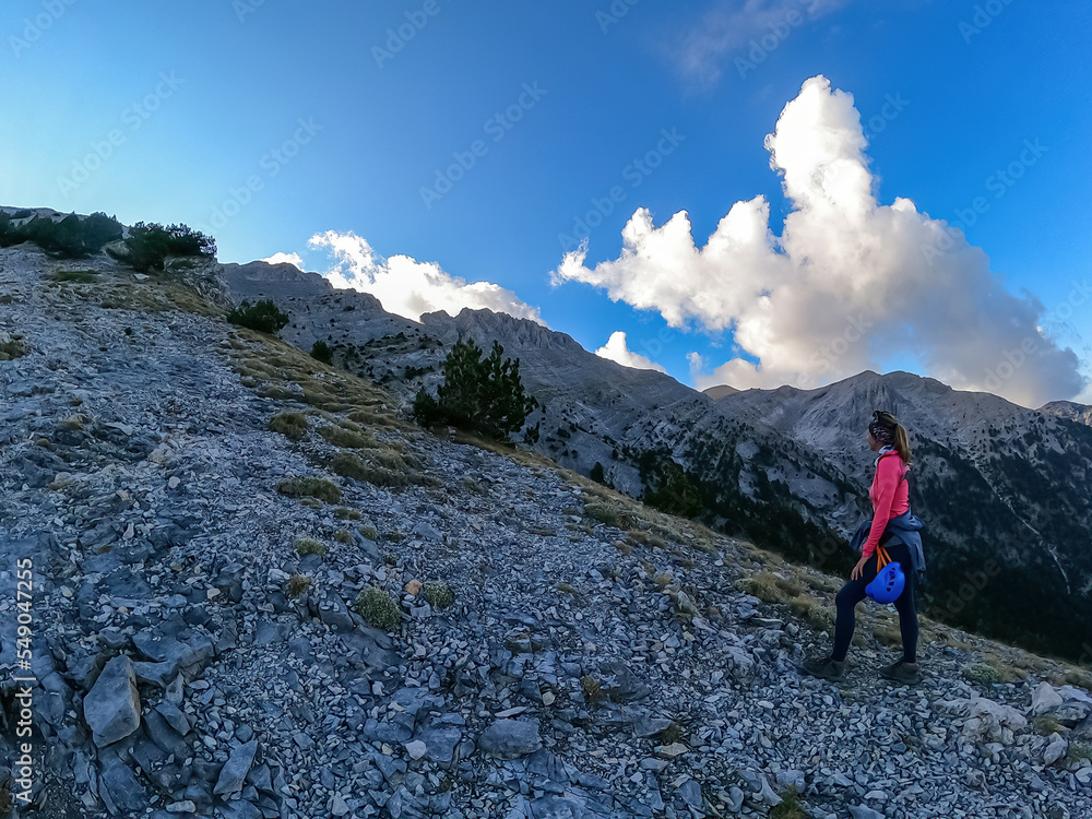 Woman climbing on mystical foggy hiking trail leading to Mount Olympus (Mytikas, Skala, Stefani) in Mt Olympus National Park, Thessaly, Greece, Europe. Scenic view of cloud covered slopes and ridges