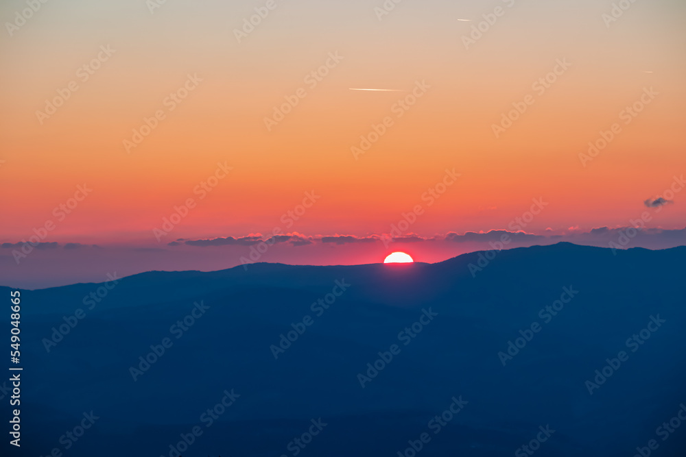 Scenic view of sun going up behind mountain Koralpe during sunrise seen from mountain peak Zingerle Kreuz, Saualpe, Lavanttal Alps, Carinthia, Austria, Europe. Soft red colored sky creating calm vibes