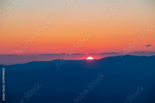 Scenic view of sun going up behind mountain Koralpe during sunrise seen from mountain peak Zingerle Kreuz  Saualpe  Lavanttal Alps  Carinthia  Austria  Europe. Soft red colored sky creating calm vibes