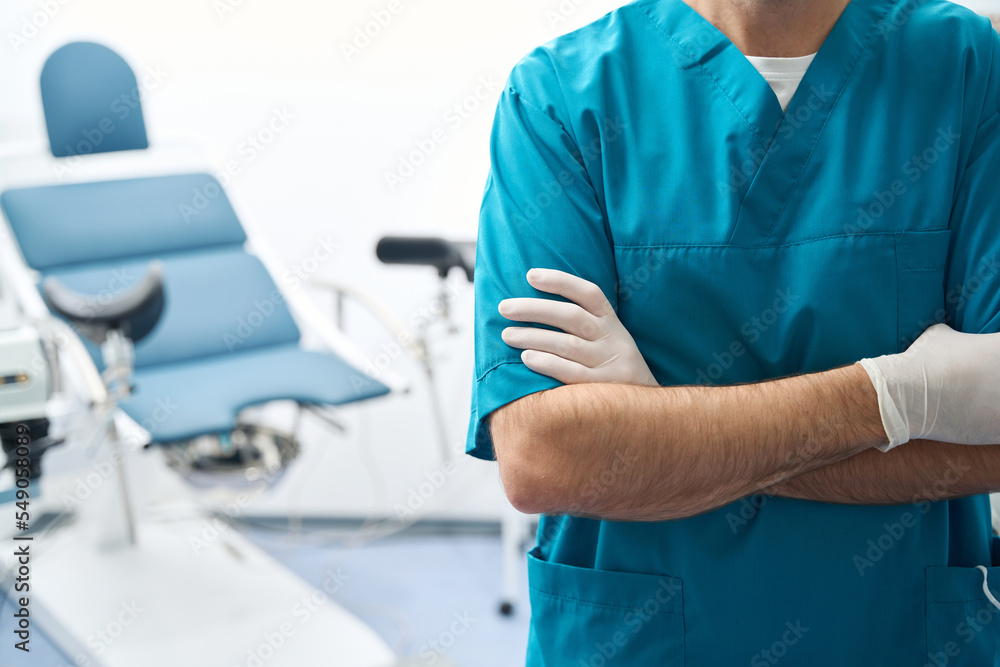 Man stands in gynecological room with arms folded across chest Man stands in gynecological room with arms folded across chest