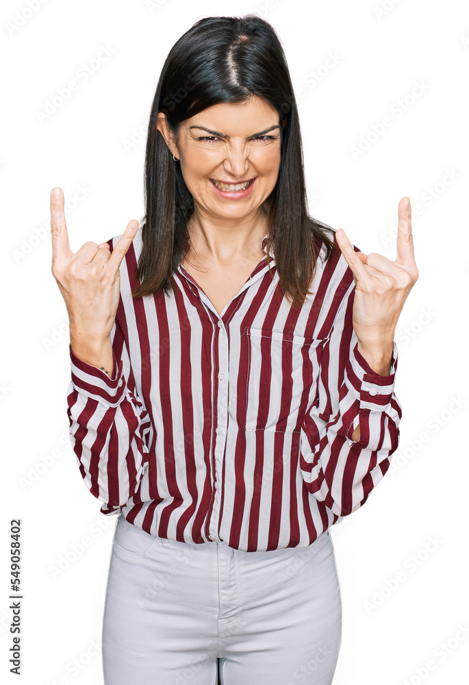 Beautiful brunette woman wearing striped shirt shouting with crazy expression doing rock symbol with hands up. music star. heavy concept. Beautiful brunette woman wearing striped shirt shouting with crazy expression doing rock symbol with hands up. music star. heavy concept.