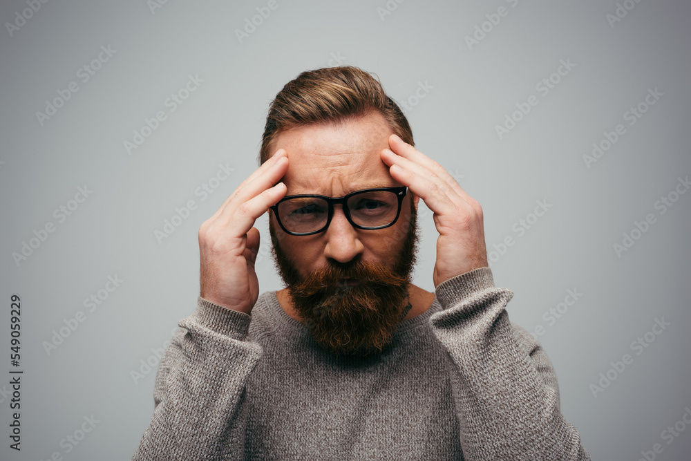 Stressed man in eyeglasses looking at camera while touching forehead isolated on grey. Stressed man in eyeglasses looking at camera while touching forehead isolated on grey.