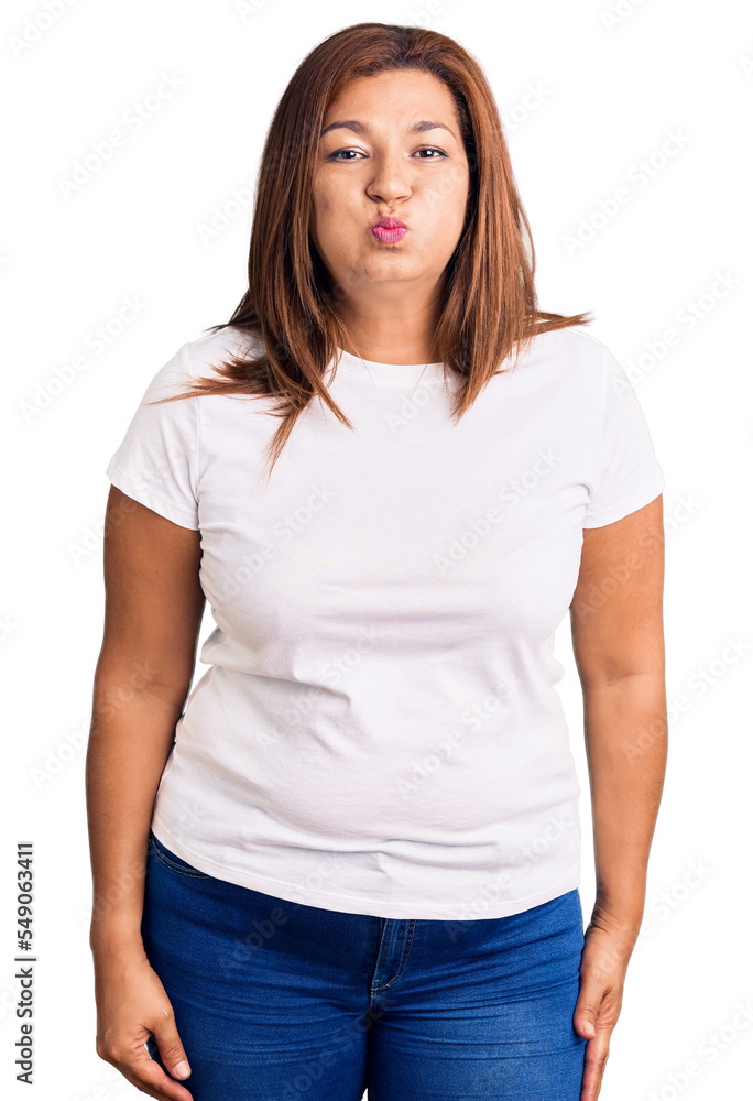 Middle age latin woman wearing casual white tshirt puffing cheeks with funny face. mouth inflated with air, crazy expression. Middle age latin woman wearing casual white tshirt puffing cheeks with funny face. mouth inflated with air, crazy expression.