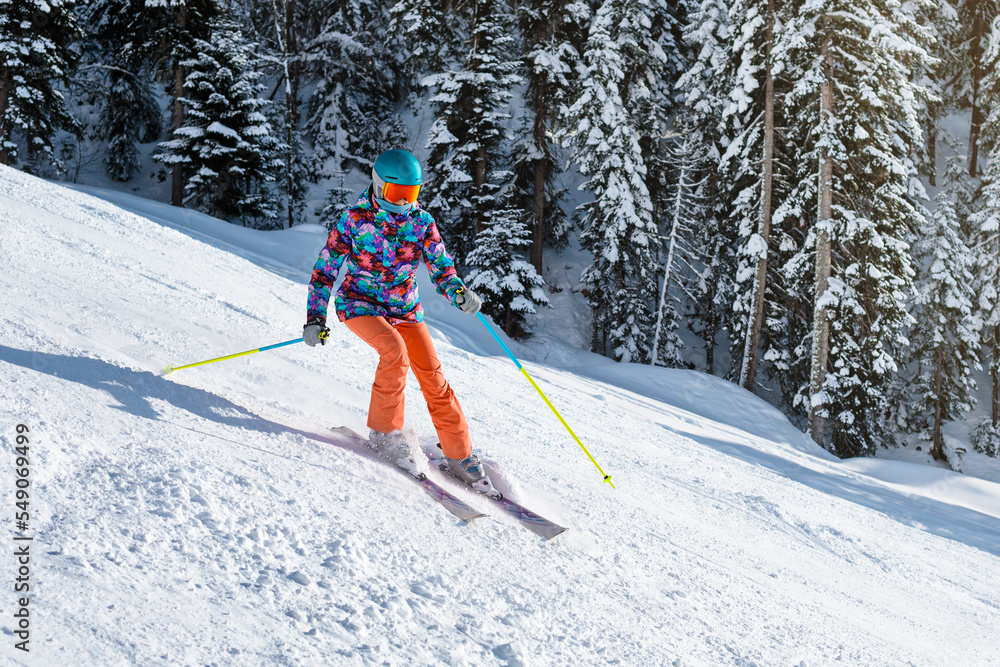 Female skier in bright clothes sliding down the slope on a sunny day at a mountain resort.
