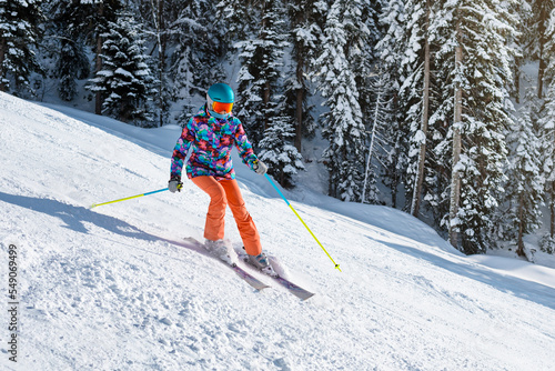 Obraz na płótnie Female skier in bright clothes sliding down the slope on a sunny day at a mountain resort. w salonie