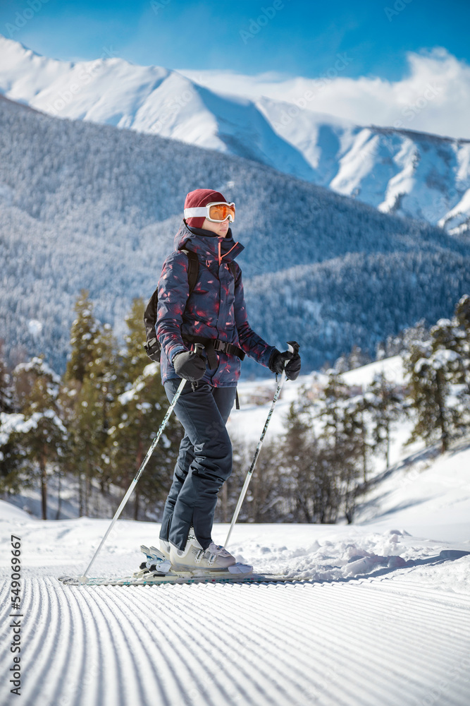 Amateur female skier enjoying the view of the mountains on the velvet slope on a sunny day at a ski resort.