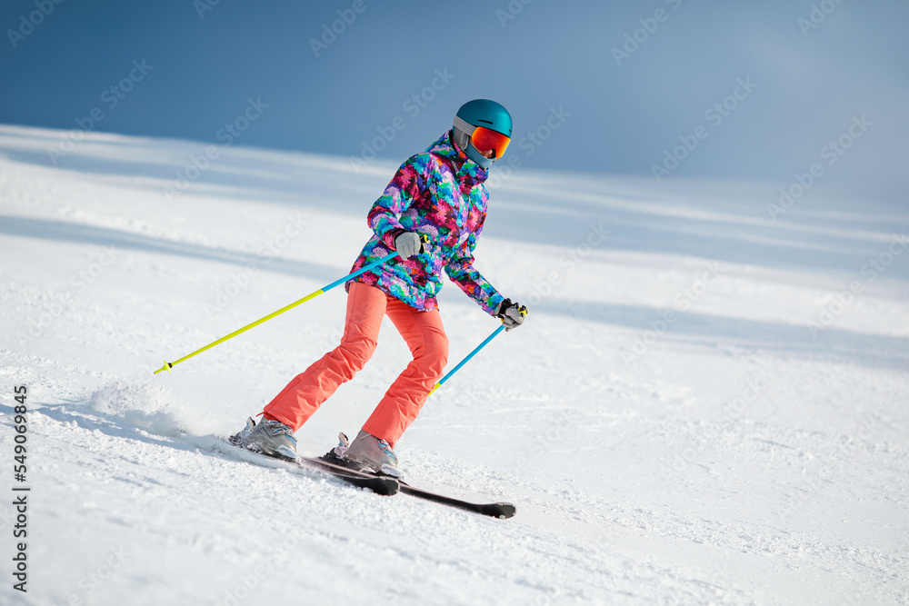 Young female skier sliding down the slope on a sunny day at a mountain resort. Copy space.