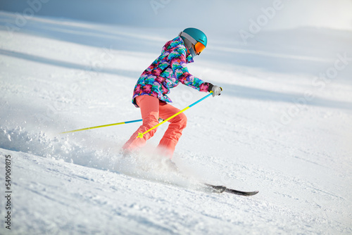 Obraz na płótnie Young female skier in colourful clothes sliding down the slope on a sunny day at a mountain resort. w salonie