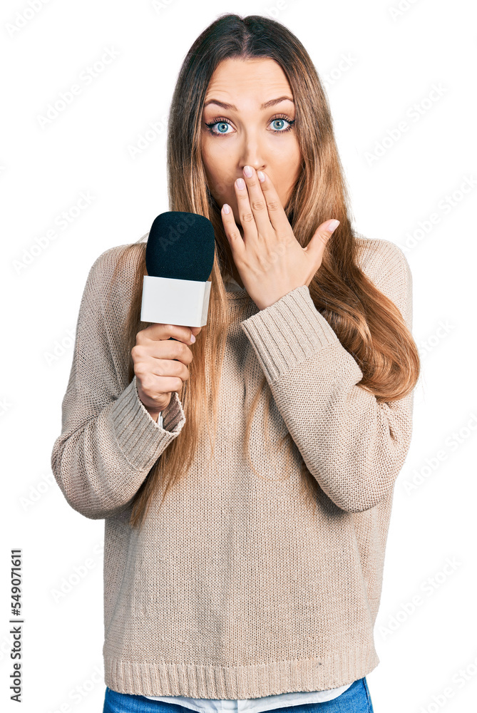 Beautiful caucasian woman holding reporter microphone covering mouth with hand, shocked and afraid for mistake. surprised expression Beautiful caucasian woman holding reporter microphone covering mouth with hand, shocked and afraid for mistake. surprised expression
