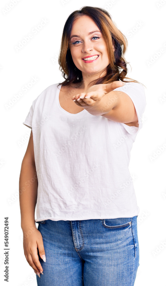 Young beautiful caucasian woman wearing casual white tshirt smiling cheerful offering palm hand giving assistance and acceptance. Young beautiful caucasian woman wearing casual white tshirt smiling cheerful offering palm hand giving assistance and acceptance.