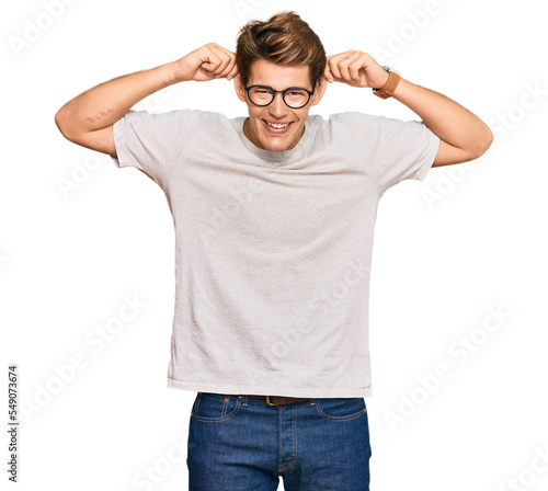 Handsome caucasian man wearing casual clothes and glasses smiling pulling ears with fingers, funny gesture. audition problem