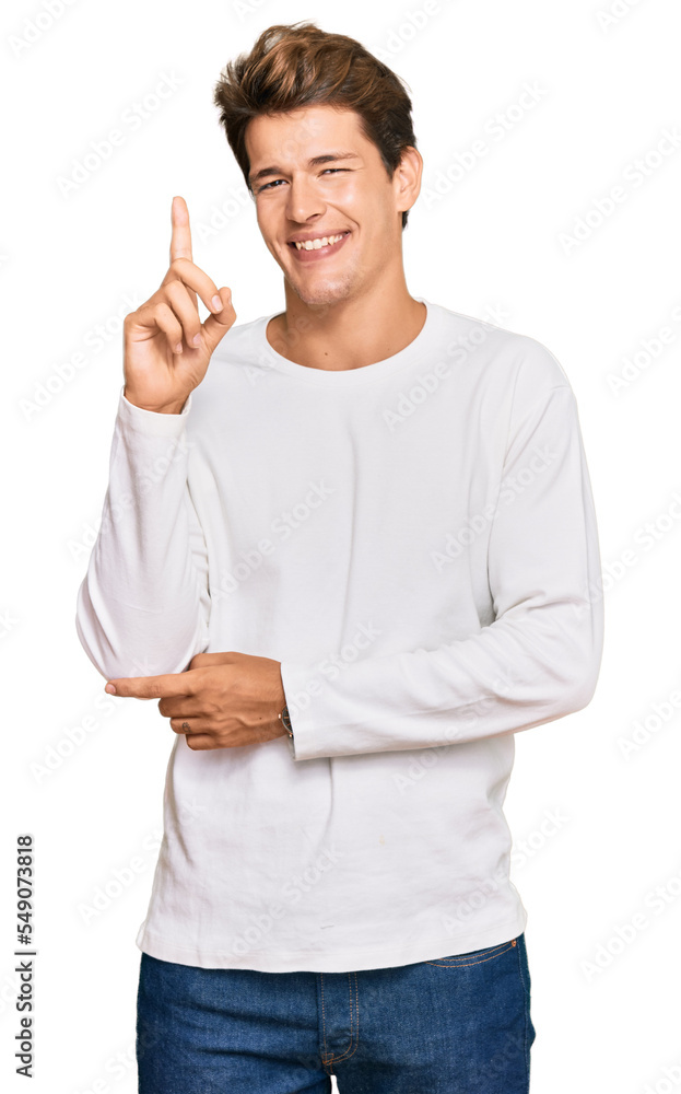 Handsome caucasian man wearing casual white sweater pointing finger up with successful idea. exited and happy. number one. Handsome caucasian man wearing casual white sweater pointing finger up with successful idea. exited and happy. number one.