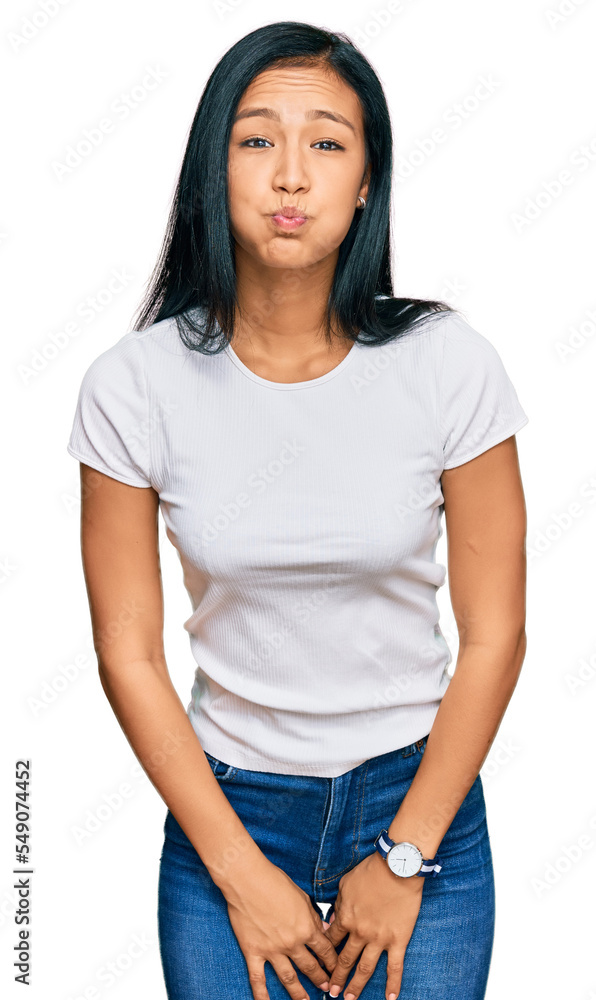 Beautiful hispanic woman wearing casual white tshirt puffing cheeks with funny face. mouth inflated with air, crazy expression. Beautiful hispanic woman wearing casual white tshirt puffing cheeks with funny face. mouth inflated with air, crazy expression.