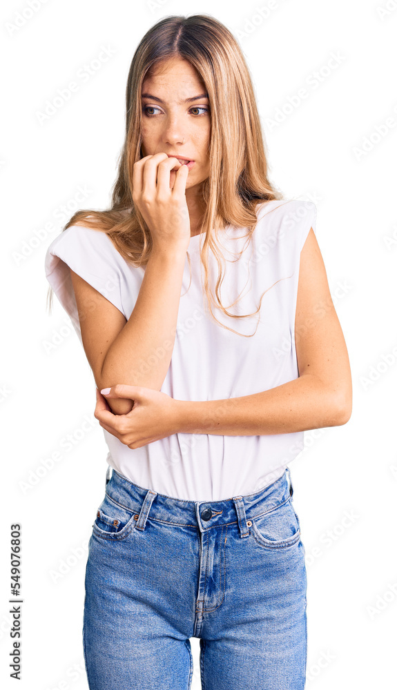Beautiful caucasian woman with blonde hair wearing casual white tshirt looking stressed and nervous with hands on mouth biting nails. anxiety problem. Beautiful caucasian woman with blonde hair wearing casual white tshirt looking stressed and nervous with hands on mouth biting nails. anxiety problem.