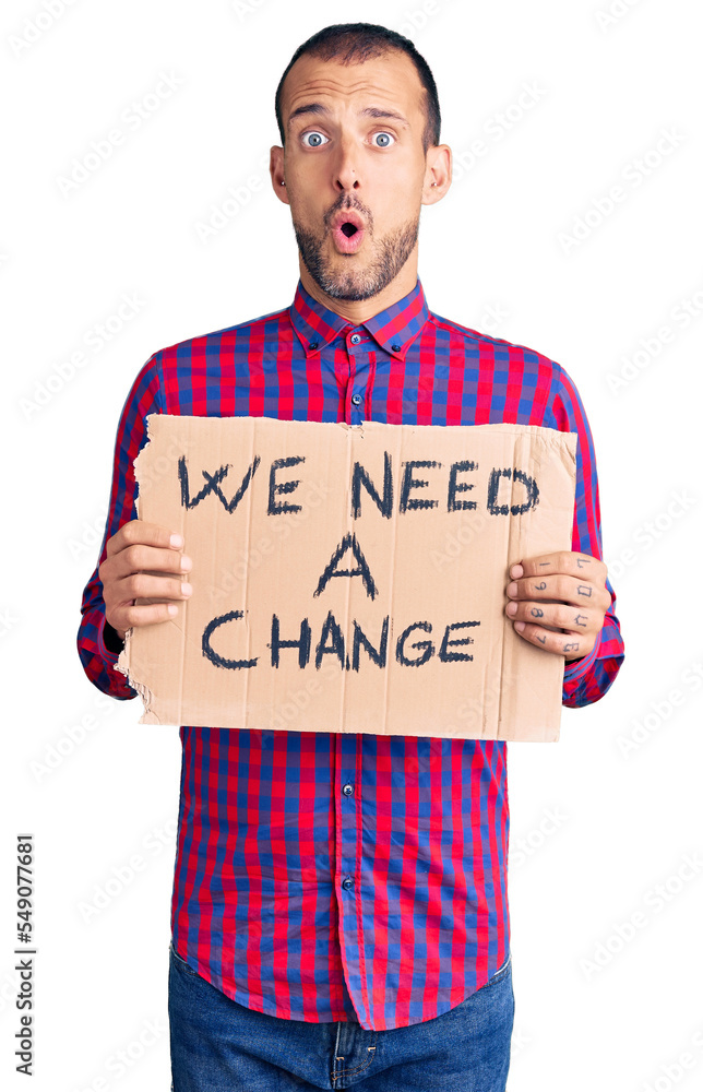 Young handsome man holding we need a change banner scared and amazed with open mouth for surprise, disbelief face Young handsome man holding we need a change banner scared and amazed with open mouth for surprise, disbelief face