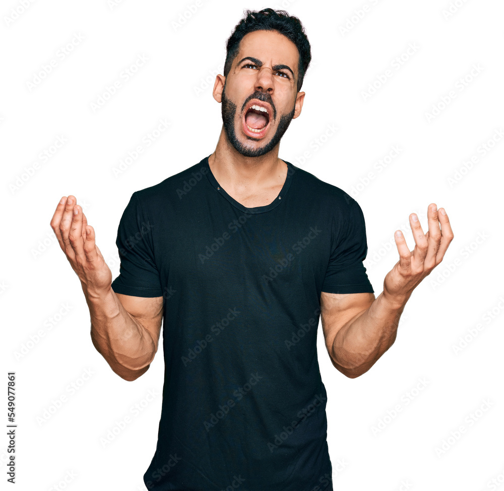 Hispanic man with beard wearing casual black t shirt crazy and mad shouting and yelling with aggressive expression and arms raised. frustration concept. Hispanic man with beard wearing casual black t shirt crazy and mad shouting and yelling with aggressive expression and arms raised. frustration concept.