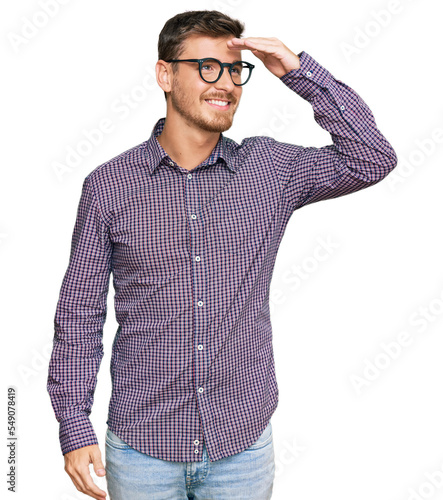 Obraz na plátně Handsome caucasian man wearing casual clothes and glasses very happy and smiling looking far away with hand over head
