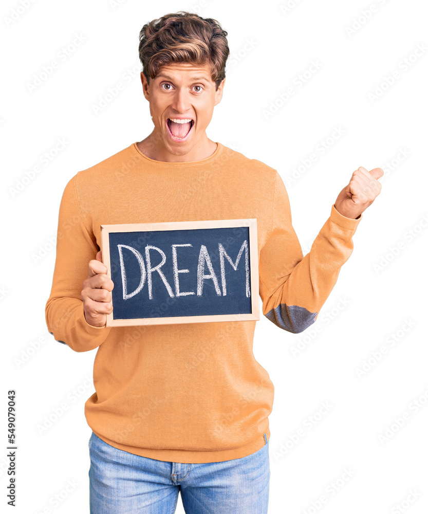 Young handsome man holding blackboard with dream word screaming proud, celebrating victory and success very excited with raised arms Young handsome man holding blackboard with dream word screaming proud, celebrating victory and success very excited with raised arms