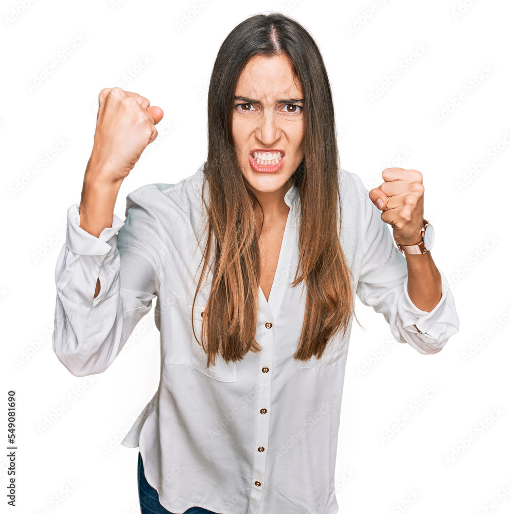 Young beautiful woman wearing casual clothes angry and mad raising fists frustrated and furious while shouting with anger. rage and aggressive concept. Young beautiful woman wearing casual clothes angry and mad raising fists frustrated and furious while shouting with anger. rage and aggressive concept.