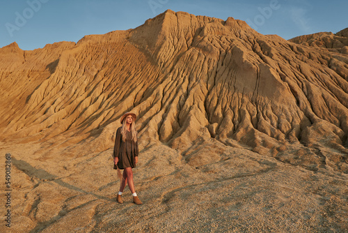 beautiful young woman wearing a hat next to a huge sandy rock. beautiful landscape and woman in the sun at sunset