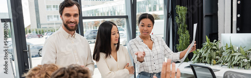 Free Download happy multiracial woman holding document and pointing with hand near multiethnic business colleagues, banner - GFXLoad