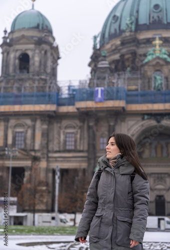 Young female tourist walking in the park in front of the Berlin Cathedral with snow all over the ground.