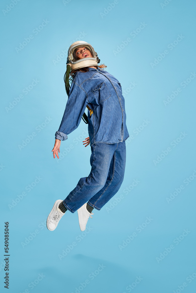 Portrait of young beautiful girl posing in uniform and astronaut helmet isolated over blue background. Jumping