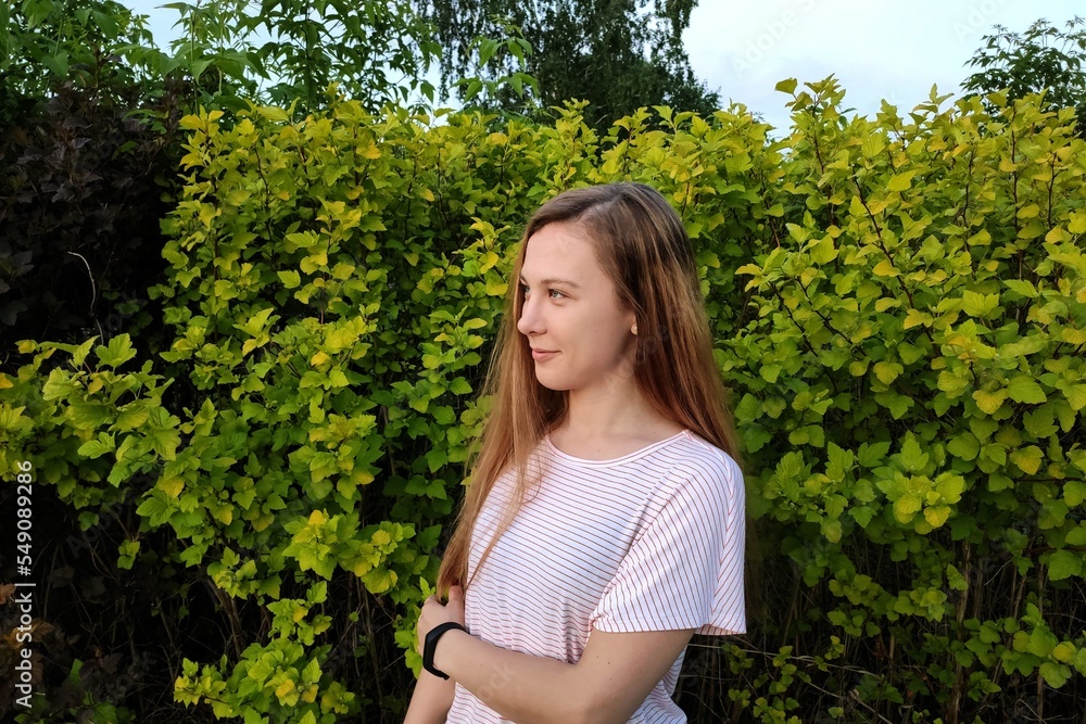 A young girl stands sideways against the background of bushes. A young girl stands sideways against the background of bushes.