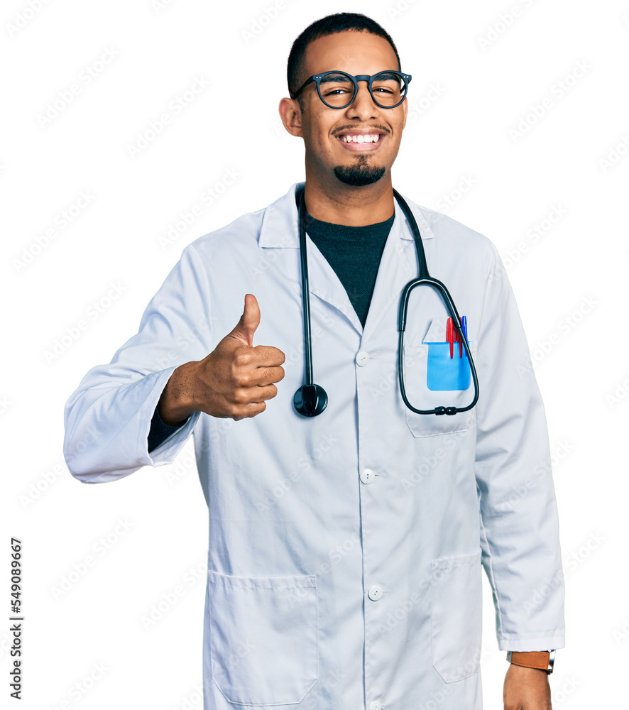 Young african american man wearing doctor uniform and stethoscope doing happy thumbs up gesture with hand. approving expression looking at the camera showing success. Young african american man wearing doctor uniform and stethoscope doing happy thumbs up gesture with hand. approving expression looking at the camera showing success.