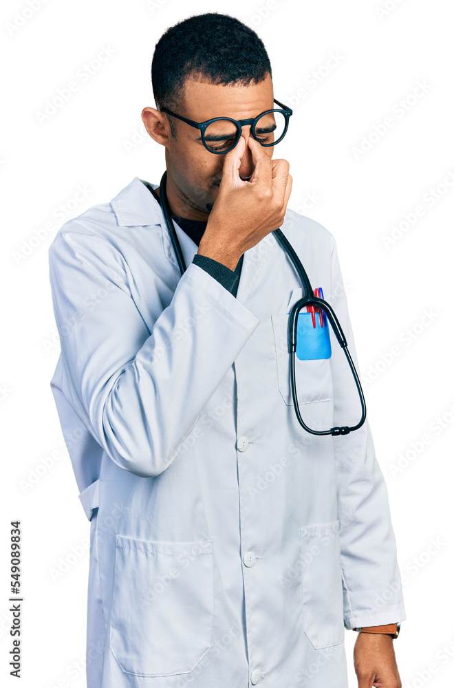 Young african american man wearing doctor uniform and stethoscope tired rubbing nose and eyes feeling fatigue and headache. stress and frustration concept. Young african american man wearing doctor uniform and stethoscope tired rubbing nose and eyes feeling fatigue and headache. stress and frustration concept.