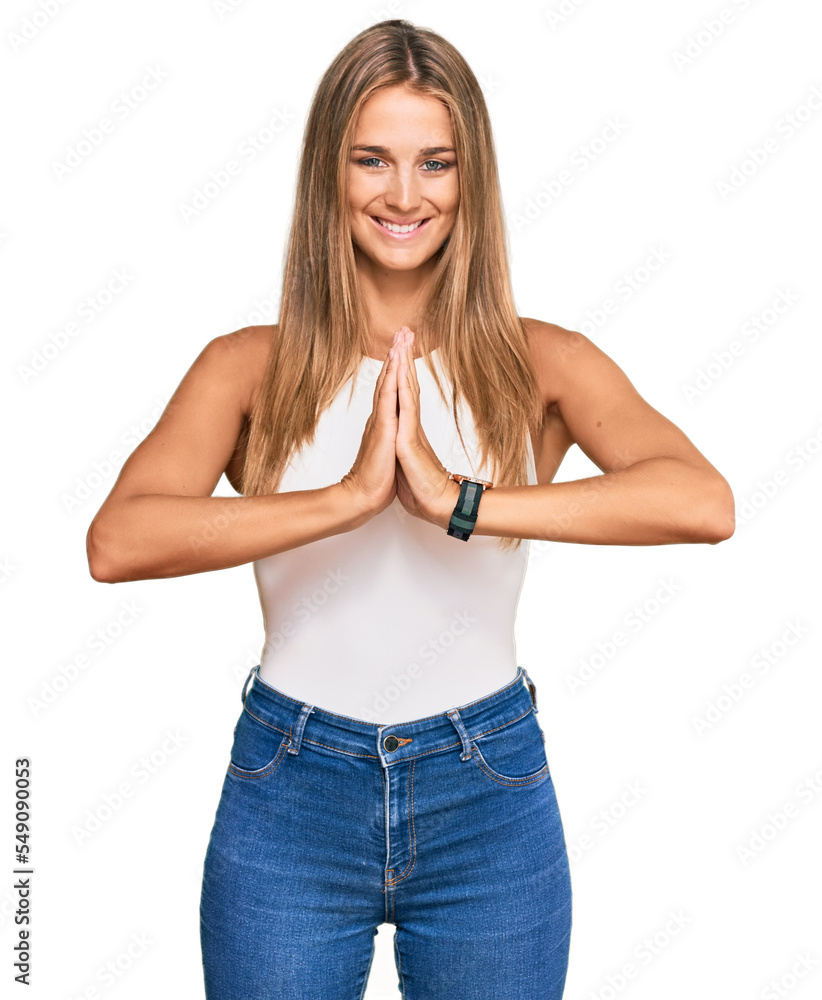Fototapeta premium Young blonde woman wearing casual style with sleeveless shirt praying with hands together asking for forgiveness smiling confident.