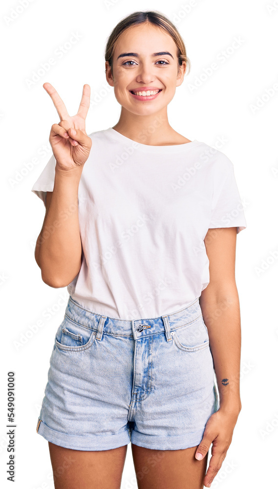 Young beautiful blonde woman wearing casual white tshirt showing and pointing up with fingers number two while smiling confident and happy. Young beautiful blonde woman wearing casual white tshirt showing and pointing up with fingers number two while smiling confident and happy.