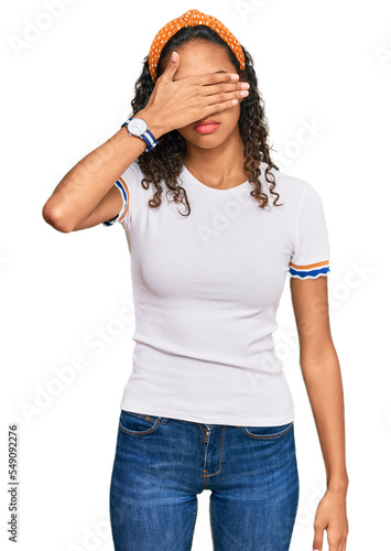 Young african american girl wearing casual clothes covering eyes with hand, looking serious and sad. sightless, hiding and rejection concept