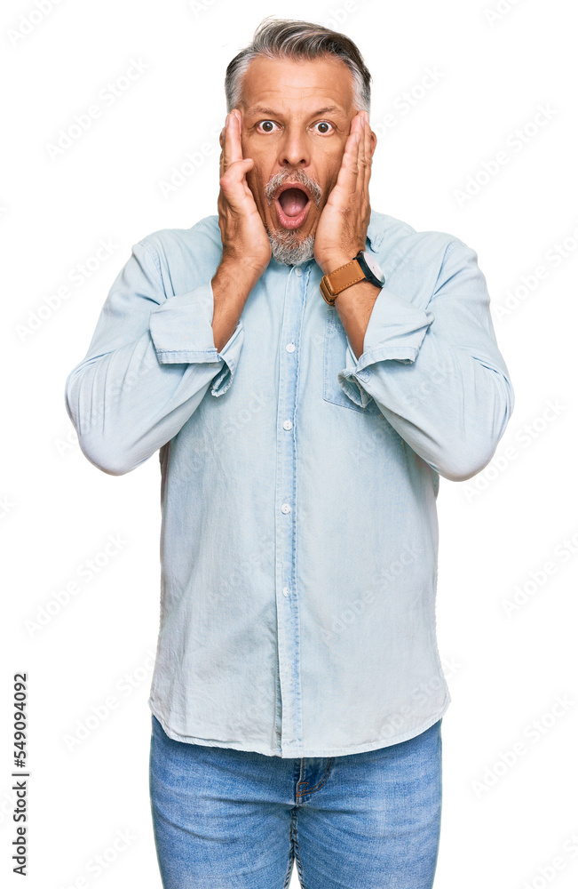 Middle age grey-haired man wearing casual clothes afraid and shocked, surprise and amazed expression with hands on face Middle age grey-haired man wearing casual clothes afraid and shocked, surprise and amazed expression with hands on face