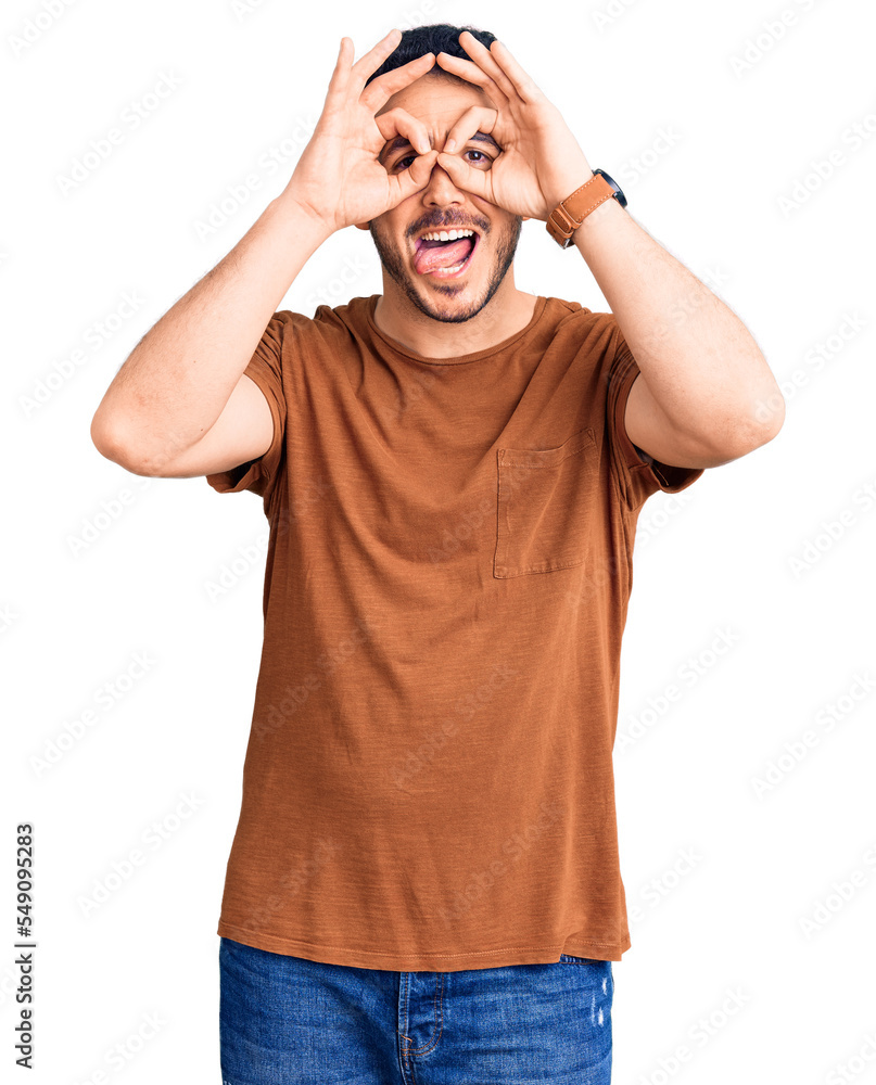 Fototapeta premium Young hispanic man wearing casual clothes doing ok gesture like binoculars sticking tongue out, eyes looking through fingers. crazy expression.