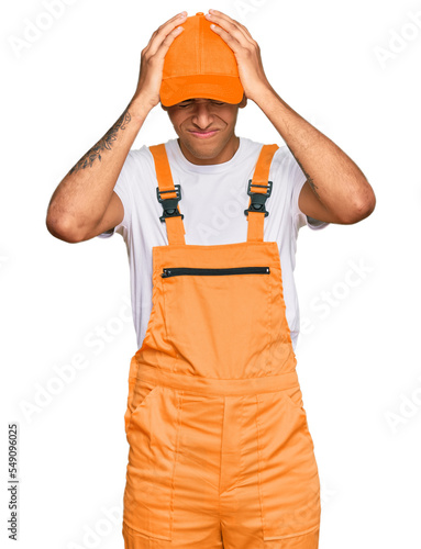 Young handsome african american man wearing handyman uniform suffering from headache desperate and stressed because pain and migraine. hands on head.