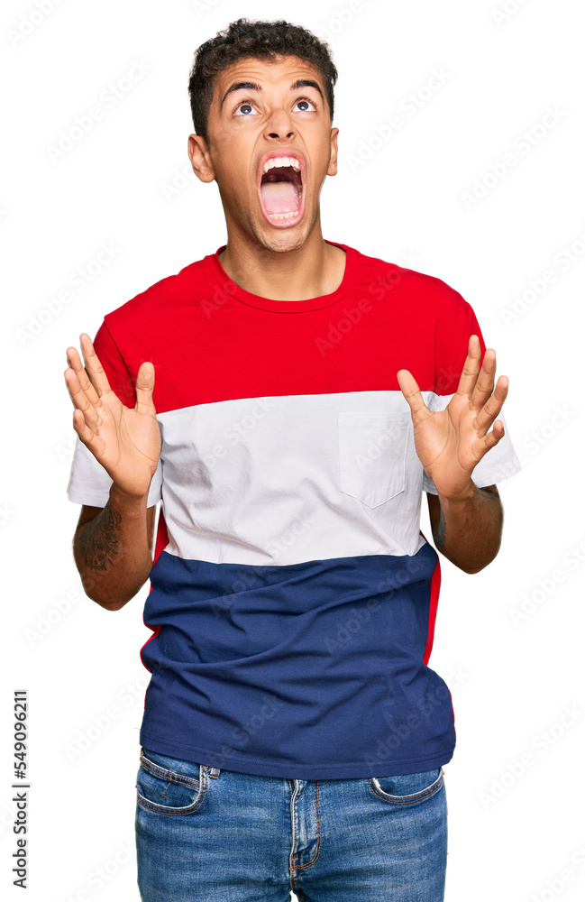 Young handsome african american man wearing casual clothes crazy and mad shouting and yelling with aggressive expression and arms raised. frustration concept. Young handsome african american man wearing casual clothes crazy and mad shouting and yelling with aggressive expression and arms raised. frustration concept.