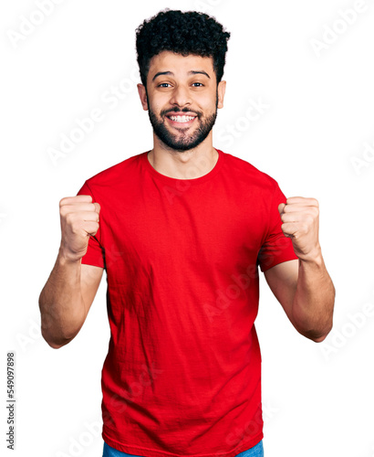 Young arab man with beard wearing casual red t shirt celebrating surprised and amazed for success with arms raised and open eyes. winner concept.