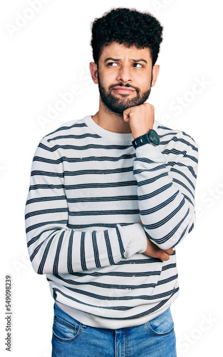 Young arab man with beard wearing casual striped sweater with hand on chin thinking about question, pensive expression. smiling and thoughtful face. doubt concept. © Krakenimages.com