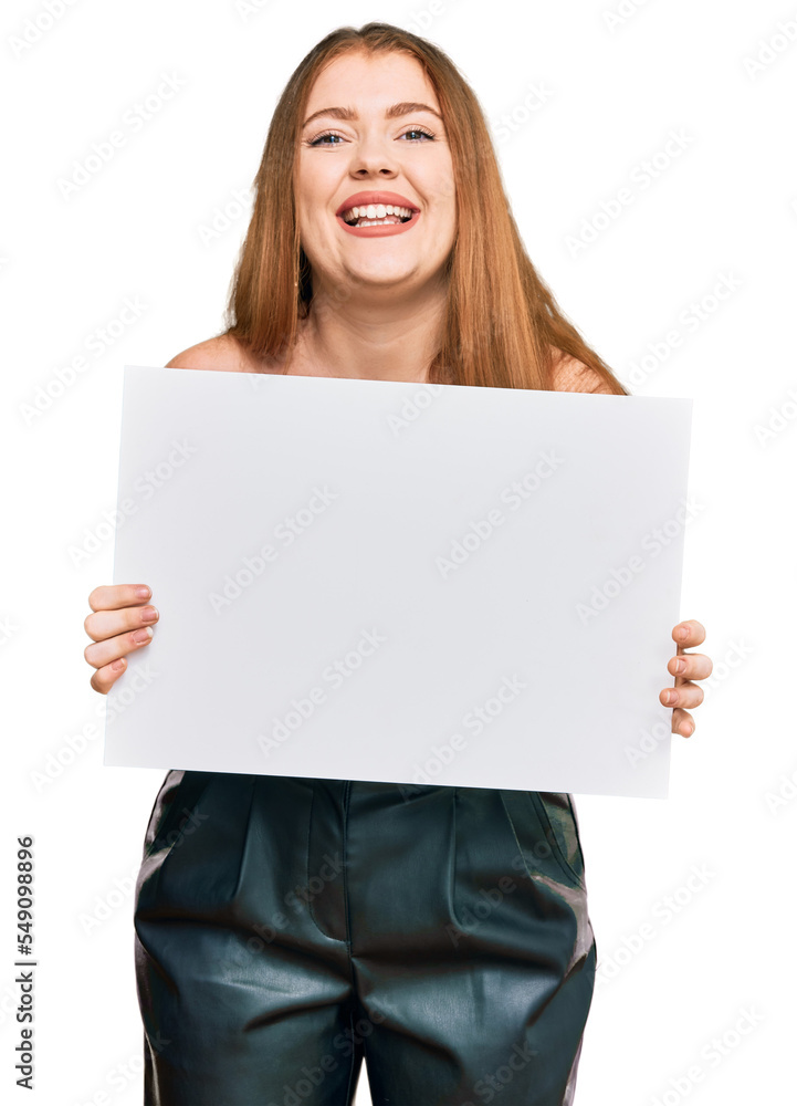 Young beautiful redhead woman holding blank empty banner looking positive and happy standing and smiling with a confident smile showing teeth Young beautiful redhead woman holding blank empty banner looking positive and happy standing and smiling with a confident smile showing teeth