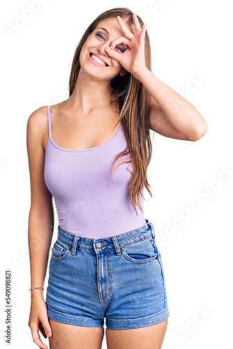 Young beautiful blonde woman wearing casual style with sleeveless shirt smiling happy doing ok sign with hand on eye looking through fingers