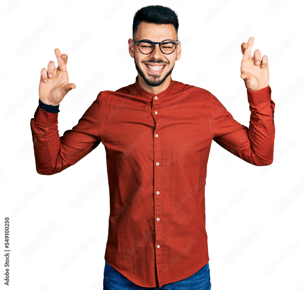Young hispanic man with beard wearing business shirt and glasses gesturing finger crossed smiling with hope and eyes closed. luck and superstitious concept. Young hispanic man with beard wearing business shirt and glasses gesturing finger crossed smiling with hope and eyes closed. luck and superstitious concept.