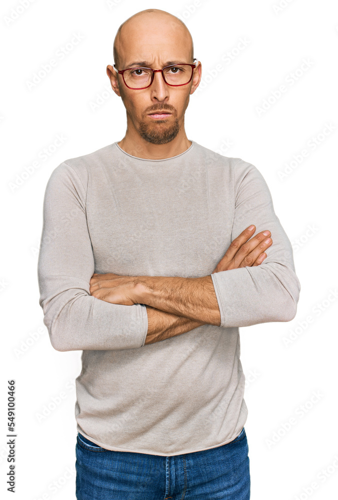 Bald man with beard wearing casual clothes and glasses skeptic and nervous, disapproving expression on face with crossed arms. negative person. Bald man with beard wearing casual clothes and glasses skeptic and nervous, disapproving expression on face with crossed arms. negative person.